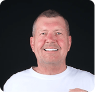 Smiling man with short hair and white shirt against black background.