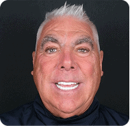 Close-up of a smiling man with white hair and bright teeth.